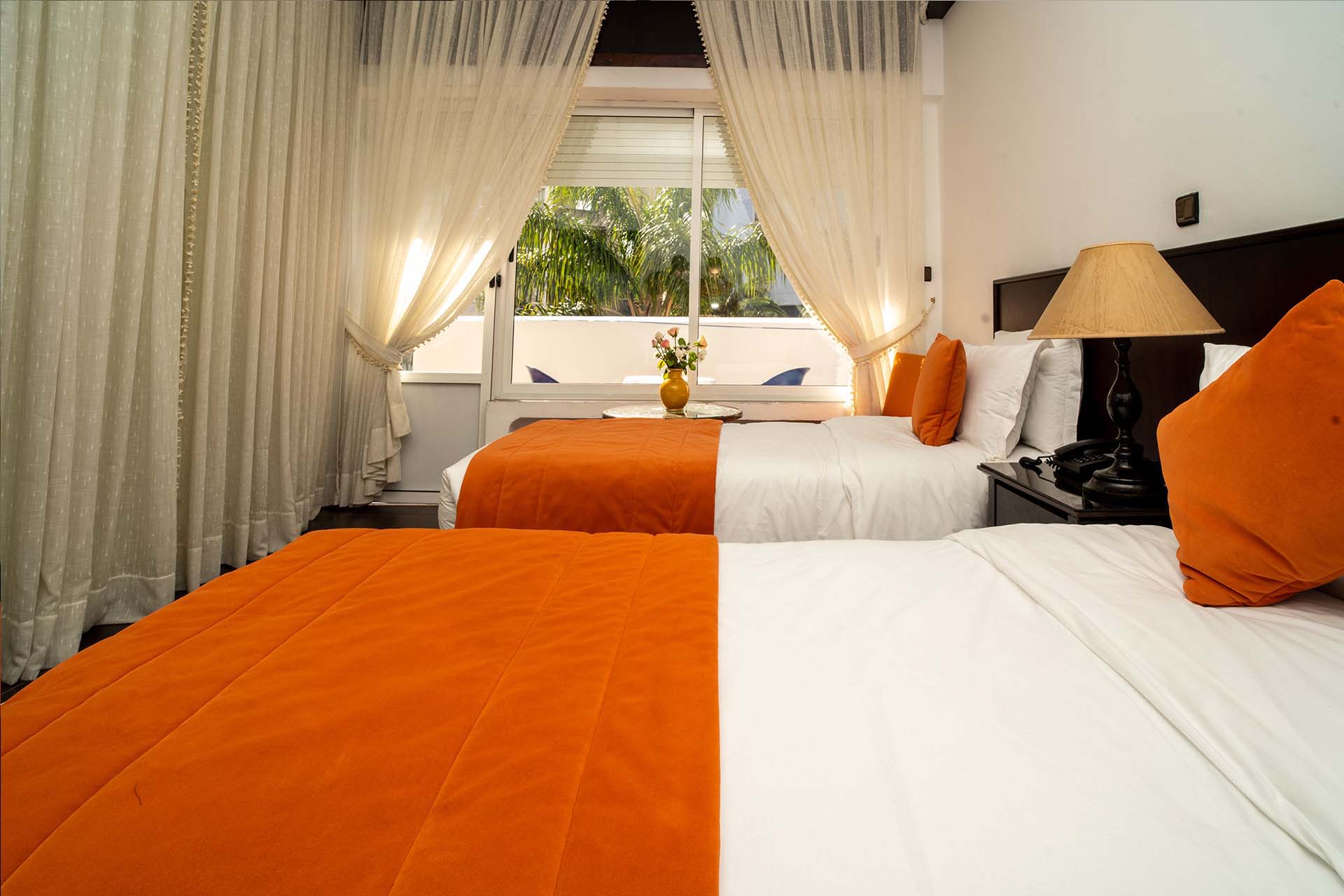Habitación con dos camas, caminos de cama naranjas y ventana orientada al jardín