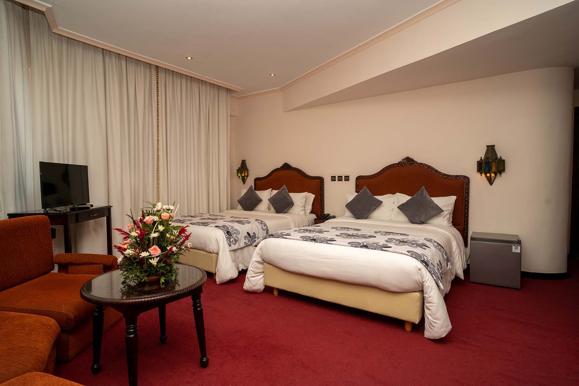 Habitación con dos camas, moqueta roja y zona de estar